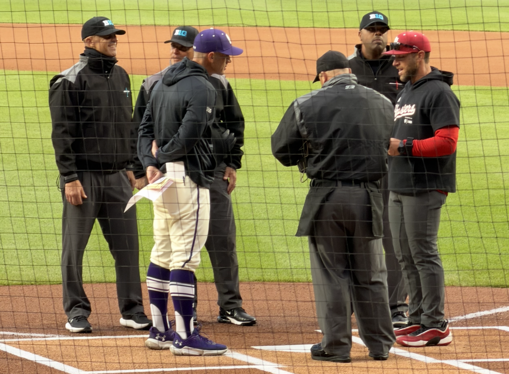Northwestern coach Ben Greenpan and Indiana coach Jeff Mercer meet with the umpires at home plate at Wrigley Field